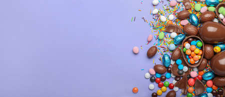 Chocolate Easter eggs with candies and sprinkles on color background with space for text