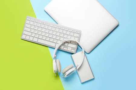Modern laptop, keyboard, headphones and power bank on color background