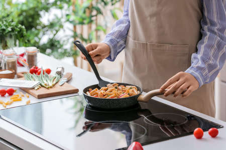 Woman cooking tasty cajun chicken pasta in kitchenの写真素材