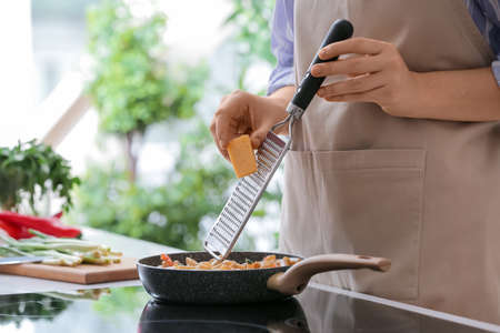 Woman grating cheese into cajun chicken pasta in kitchenの写真素材