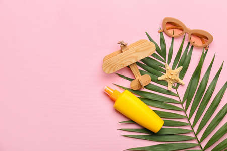 Composition with stylish sunglasses, wooden plane, bottle of sunscreen and palm leaf on pink...