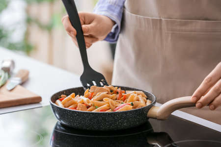 Woman cooking tasty cajun chicken pasta in kitchenの写真素材