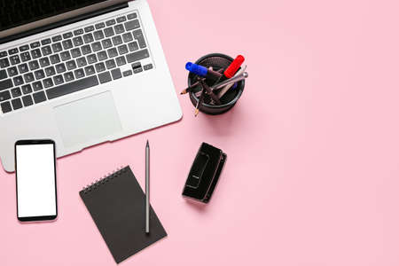 Modern laptop, mobile phone and stationery on pink backgroundの写真素材