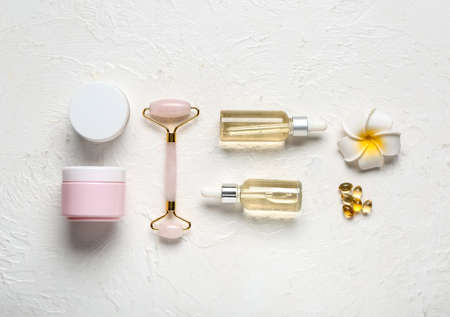 Composition with bottles of essential oil, cosmetics and facial massage tool on light backgroundの写真素材