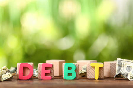 Word DEBT with cubes and money on table outdoors