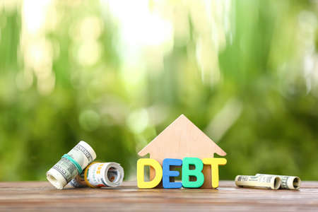 Word DEBT with house figure and money on table outdoorsの写真素材