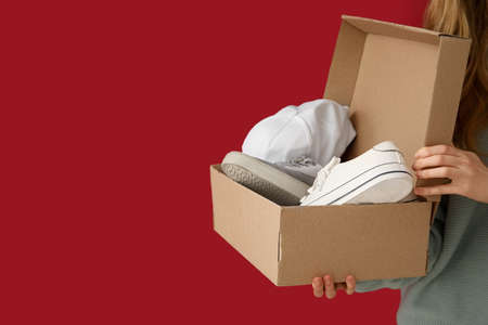 Woman and wardrobe box with clothes on color background
