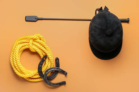 Horse riding helmet and crop with rope and horseshoes on color background