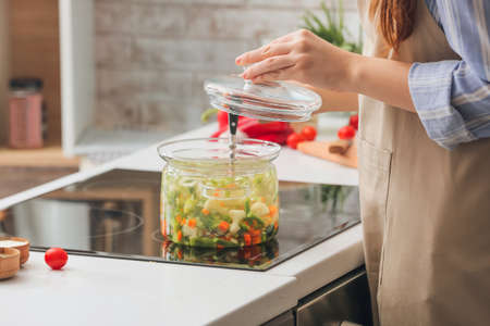 Woman making tasty dietary soup on electric stove in kitchenの写真素材