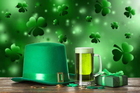 Leprechaun's hat, gift box and glass of beer on table against green background. St. Patrick's Day...