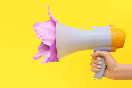 Woman with megaphone and gladiolus flower on yellow backgroundの写真素材
