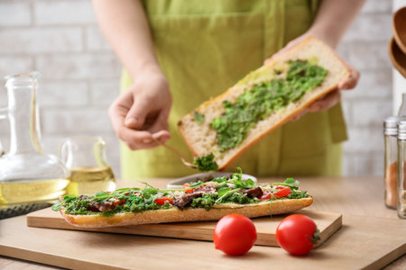 Woman preparing tasty sandwich with pesto sauce in kitchenの写真素材
