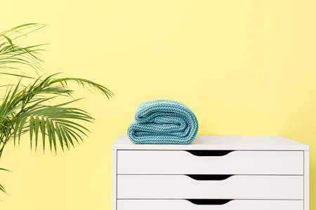Knitted plaid on chest of drawers near color wallの写真素材