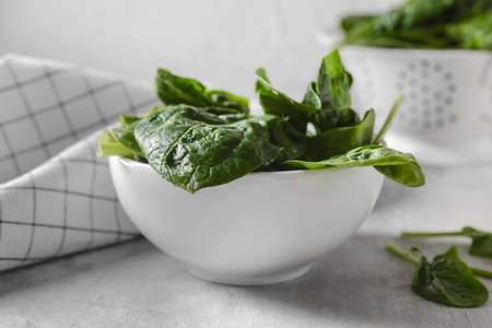 Bowl with fresh spinach leaves on light background, closeup