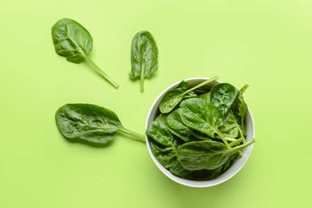 Bowl with fresh spinach leaves on color background