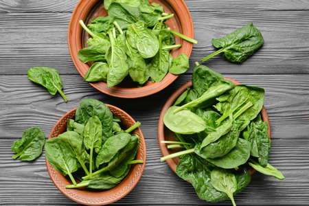 Plates with fresh spinach leaves on wooden background