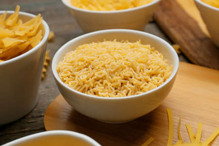 Bowl with uncooked alphabet pasta on wooden background