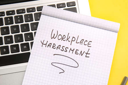 Notebook with text WORKPLACE HARASSMENT and laptop on color backgroundの写真素材