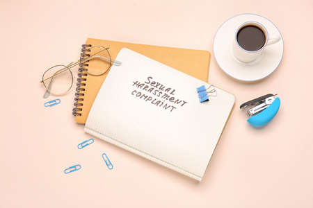 Stationery with text SEXUAL HARASSMENT COMPLAINT and cup of coffee on color background