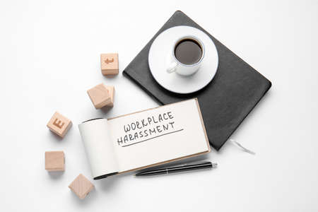 Notebook with text WORKPLACE HARASSMENT, cubes and cup of coffee on white background