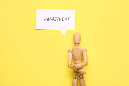 Paper with word HARASSMENT and wooden mannequin on color background