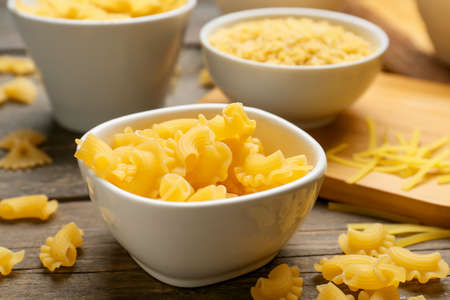Bowl with uncooked creste pasta on wooden background