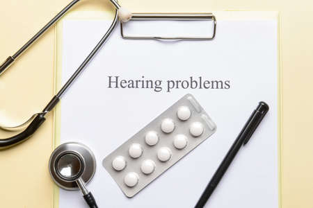 Clipboard with text HEARING PROBLEMS and pills on color background