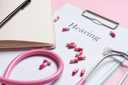 Clipboard with word HEARING, stethoscope and pills on color backgroundの写真素材