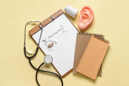 Clipboard with text HEARING LOSS, stethoscope and pills on color backgroundの写真素材