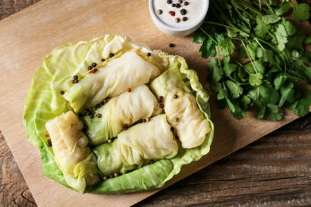 Board with uncooked cabbage rolls on wooden background