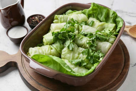 Baking dish with uncooked cabbage rolls and parsley on light background