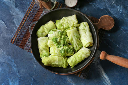 Frying pan with uncooked cabbage rolls on color background
