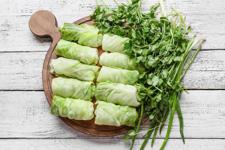 Tray with uncooked cabbage rolls on light wooden background
