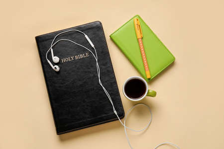 Holy Bible, earphones, cup of coffee and notebook on color backgroundの写真素材