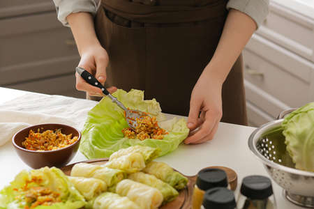Woman preparing stuffed cabbage rolls on table in kitchen, closeupの写真素材