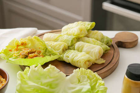 Wooden board with raw stuffed cabbage rolls on table in kitchen