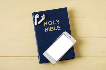 Holy Bible, earphones and mobile phone on color wooden background