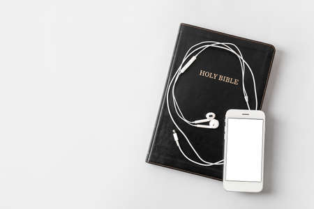 Holy Bible, mobile phone and earphones on light background