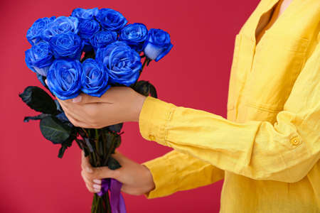 Woman with beautiful blue roses on color background