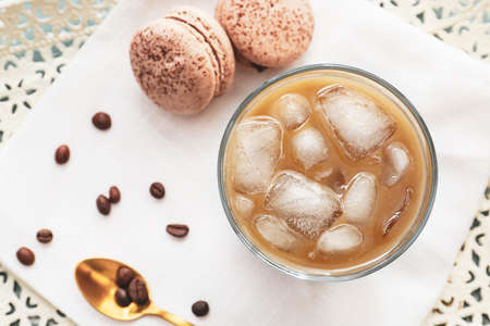 Glass of tasty iced coffee and macaroons on tray