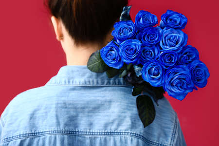 Woman with beautiful blue roses on color background
