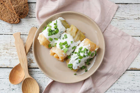 Plate with tasty stuffed cabbage rolls and sauce on light wooden background