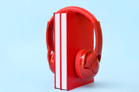 Modern headphones with books on color background