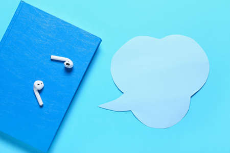 Modern earphones with book and speech bubble on color background