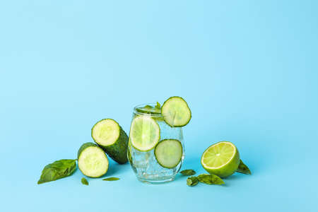 Glass with cucumber lemonade on color background
