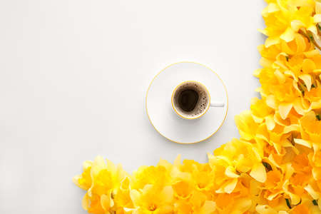 Cup of coffee and beautiful daffodils on light backgroundの写真素材