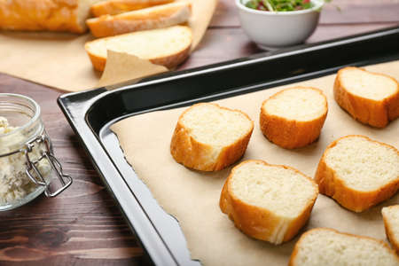 Baking sheet with slices of fresh bread on wooden table