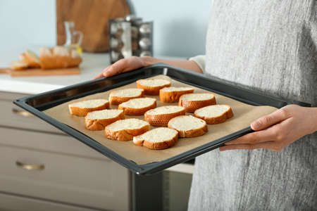 Female chef holding baking sheet with slices of fresh bread in kitchen, closeup