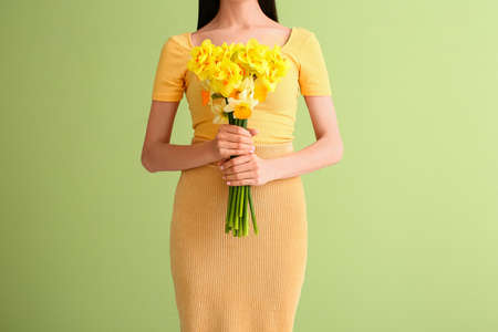 Beautiful young woman with narcissus bouquet on color background