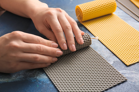 Woman making wax candles on color background, closeup